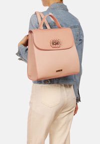 Zaino in pelle rosa chiaro con un design strutturato, manico superiore e chiusura decorativa. Tessuto morbido e dettaglio di branding minimalista.