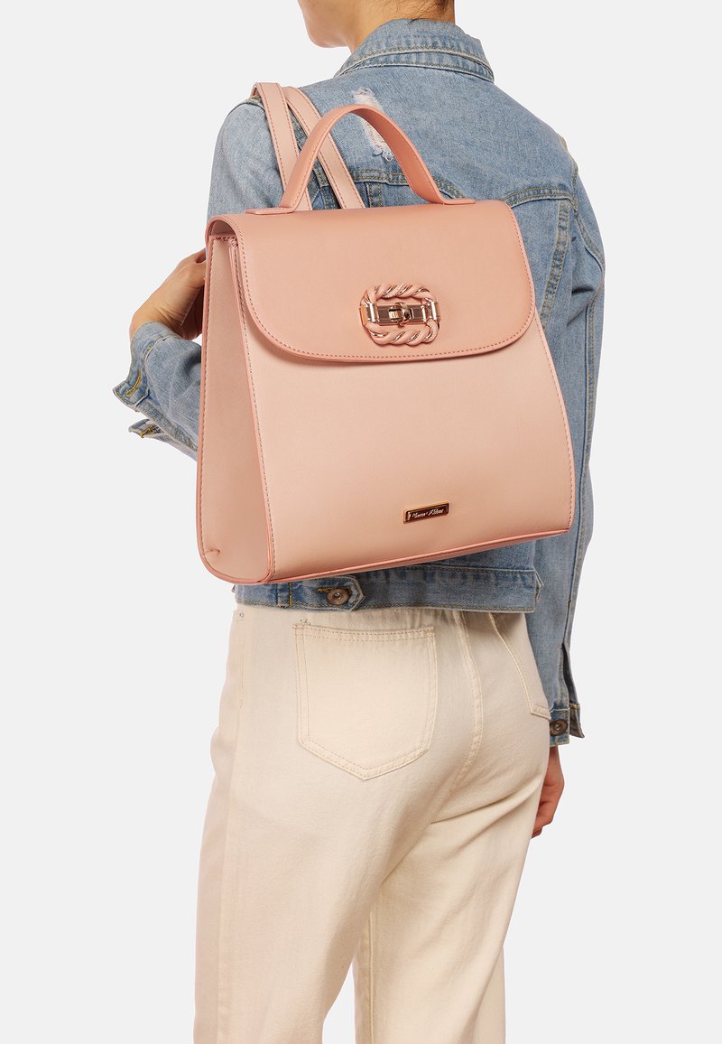 Zaino in pelle rosa chiaro con un design strutturato, manico superiore e chiusura decorativa. Tessuto morbido e dettaglio di branding minimalista.