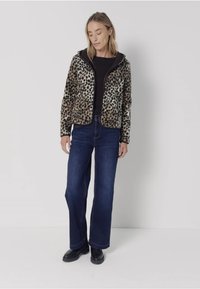 Leopardmönstrad fuskpälsjacka med dragkedja, i kombination med en svart topp och löst sittande mörk denimjeans. Svarta ankelstövlar fulländar outfiten.