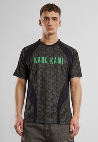 Tamsiai pilka trumpų rankovių sportinė marškinėliai su žaliu "KARL KANI" logotipu. Yra tekstūruotas raštas ir juodos detalės šonuose.