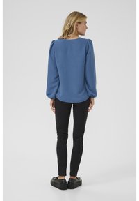 Blauer strukturierter Oberteil mit Puffärmeln, kombiniert mit schwarzen, eng anliegenden Jeans und schwarzen Plateauschuhen. Einfacher runder Ausschnitt und lockere Silhouette.