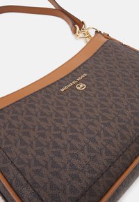 Svart och brun Michael Kors axelväska med ett geometriskt mönster, ljusbruna läderdetaljer, guldlogotyp och justerbar rem.