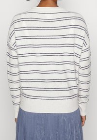 Vit tröja med marinblå horisontella ränder, rund hals och ribbade ärmslut. Matchad med en plisserad blå kjol. Mjuk textur och avslappnad design.