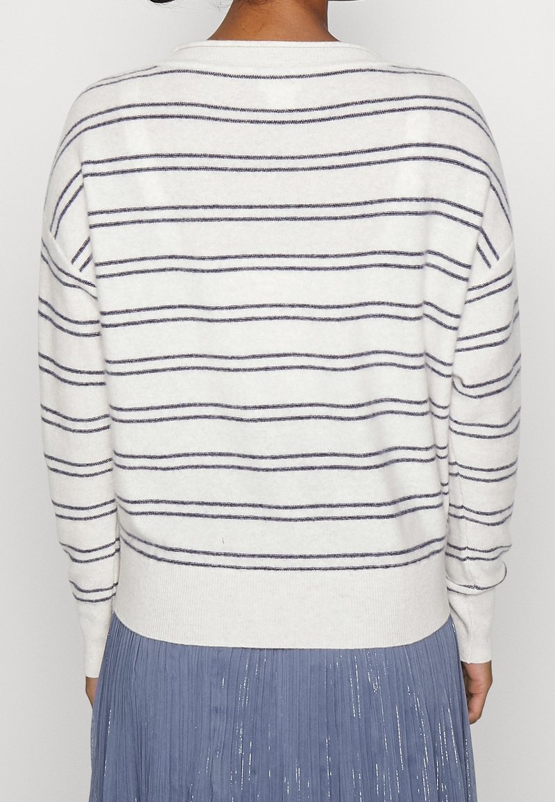 Vit tröja med marinblå horisontella ränder, rund hals och ribbade ärmslut. Matchad med en plisserad blå kjol. Mjuk textur och avslappnad design.