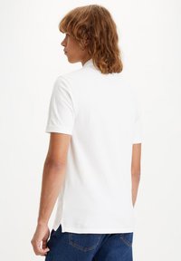 White cotton short-sleeve t-shirt with a classic fit, featuring a ribbed collar and side slits, seen from the back against a plain background.