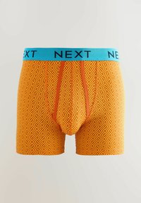 Boxer-culottes orange avec un motif géométrique en losanges, dotées d'une taille élastique bleue portant l'inscription "NEXT". Tissu doux avec un design ajusté.