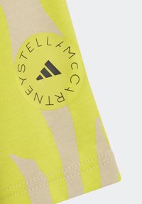 Ljusgul tyg med ett beige abstrakt mönster. Inkluderar en cirkulär svart logotyp med "Stella McCartney" och ett design med tre ränder.