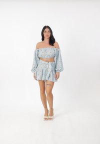 Top corto a spalle scoperte, di un delicato azzurro floreale, con maniche a sbuffo, abbinato a una gonna avvolgente coordinata. Il tessuto è morbido con una sottile trama.