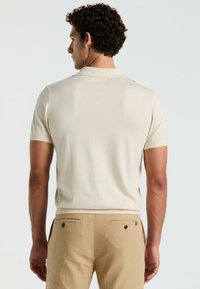 Licht beige poloshirt met korte mouwen, ribbelkraag en een subtiele textuur, gecombineerd met tan linnen broek met achterzakken.