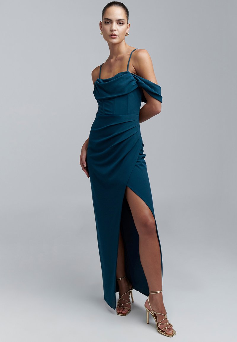 Sinisenvihreä satiininen iltapuku, jossa olkaimeton malli, sivuhalkio, ryppyinen yksityiskohta ja ohuet hihnat. Yhdistetty kultaisiin remmikenkiin.