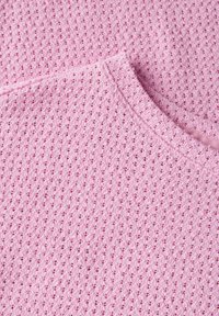 Haut tricoté rose clair avec un motif texturé à petits trous, un col rond et une bordure côtelée le long des bords.