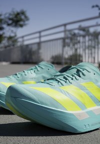 Light blue running shoes with bright yellow accents and textured upper. Features prominent three-stripe design and cushioned sole.