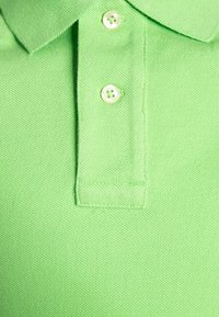 Ljusgrön polo skjorta i texturerat tyg, med klassisk krage, två vita knappar och en sydd fåll.