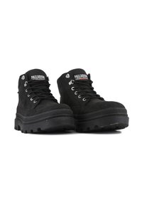 Botas de tobillo de ante negro con suela de goma gruesa, ojales de metal y cuello acolchado. Presenta una franja de goma texturizada a lo largo de la suela.