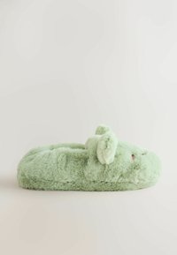 Zapatilla de felpa verde con textura suave, forma redondeada y pequeños acentos de orejas. Cuenta con detalles cosidos y una soletera cómoda y acolchada.