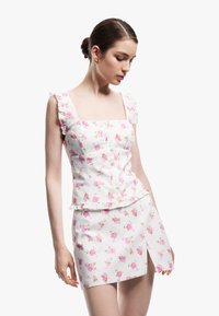 Blomstret top og nederdel sæt i hvid, med lyserøde roser, flæser på stropperne, firkantet neckline og et tætsiddende design med en sideslids.