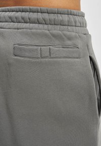 Pantalones cortos deportivos grises hechos de tela suave, con una cintura elástica y un bolsillo horizontal en la parte trasera con un detalle sutil de costura.