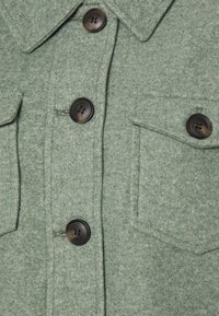 Green wool-blend jacket featuring four black buttons, dual chest pockets, a pointed collar, and a textured, soft finish.