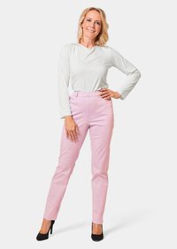 Lichte, langdurige witte blouse gecombineerd met hoogwaardige, strakke roze broeken. De outfit wordt aangevuld met zwarte hoge hakken.