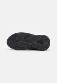 Suola di sneakers nera con un design in gomma testurizzata, caratterizzata da profonde scanalature e un logo impresso. Le forme curve e i motivi migliorano la presa.