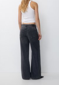 Wide-leg black jeans featuring a high waist, five-pocket design, and a stitched waistband patch. Fabric has a smooth texture with light fading.