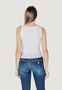 Top bianco senza maniche con un design aderente, dotato di scollatura rotonda e piccolo dettaglio del logo sul retro, abbinato a jeans in denim blu.