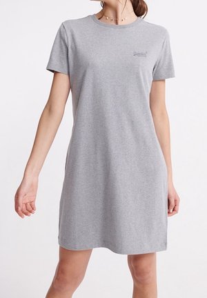 Femme portant une robe t-shirt grise à manches courtes et longueur genou, avec un logo subtil sur la poitrine.