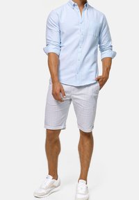 Chemise bleu clair à manches longues avec une poche poitrine, associée à un short blanc à motifs et des baskets blanches.