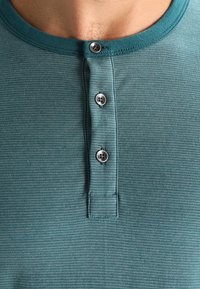 Türkisfarbendes Baumwoll-Henley-Shirt mit gerippter Textur, ausgestattet mit einer Drei-Knopf-Leiste und einem runden Ausschnitt.