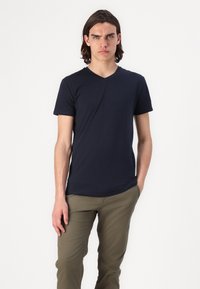 T-shirt blu navy a maniche corte con scollatura a V realizzata in tessuto morbido, abbinata a pantaloni slim-fit verdi oliva, caratterizzati da un design semplice e una superficie liscia.