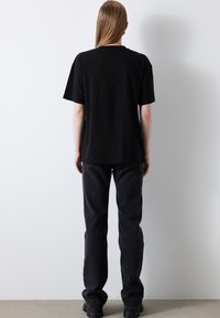 Černé bavlněné tričko s krátkým rukávem, rovného střihu a kulatým výstřihem, spárované s tmavými džínami a masivními černými botami.