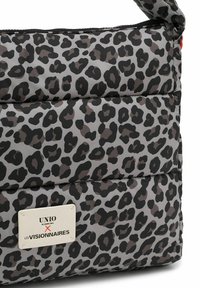 Ecke einer gepolsterten Tasche mit grauem und schwarzem Leopardenmuster und einem weißen rechteckigen Aufnäher mit der Aufschrift "UNIO Hamburg x Les Visionnaires".