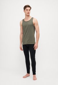 Olajzöld ujjatlan póló, kerek nyakkal, feketére igazított leggings-szel párosítva. Mindkét ruhadarab puha, rugalmas anyagból készült.