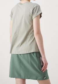 Ljusgrön bomullströja med rullade ärmar, kombinerad med en mörkgrön kjol med en sidoficka och två dekorativa ränder.