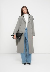 Cappotto lungo grigio con grandi bottoni e patte, abbinato a jeans a gamba larga blu chiaro e una borsa a tracolla nera.