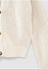 Kremowy sweter na guziki z dzianiny o fakturowanym wzorze, z prążkowanymi mankietami i dołem oraz dużymi brązowymi guzikami z przodu.