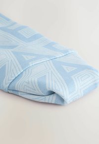 Svetlo modrý šál s geometrickými vzormi v texturovom úplete. Prehnutý, ukazujúci zložitý dizajn a hladký, jemný materiál.