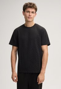 Schwarzes T-Shirt aus strukturiertem Stoff mit Rundhalsausschnitt und kurzen Ärmeln, das ein dezentes Diamantmuster aufweist.