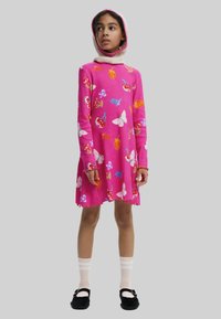 Helles pinkes Kleid mit langen Ärmeln, das mit bunten Frucht- und Schmetterlingsmustern, einem gewellten Saum und einer abnehmbaren Kapuze ausgestattet ist. Tragen Sie dazu knielange Socken und schwarze Schuhe.