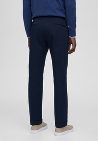 Pantalones navy de corte ajustado, con dobladillos en los extremos y dos bolsillos traseros. El material parece suave con una textura sutil. Combinados con zapatillas beige.