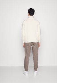 Stickad, krämfärgad pullover med hög krage, i kombination med mjuka, beige joggers och vita sneakers; slät textur och avslappnad passform.