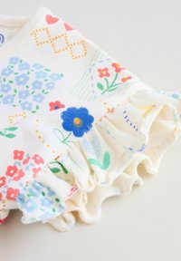 Valge kangas erkroosade lillemotiividega, millel on volangidega servad ja peened tekstuurid. Detailides on punased, sinised ja rohelised lilled.