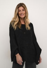 Svart stickad tröja med en lös design och vågmönster samt vida �ärmar. Strukturerat tyg med ribbade muddar och rund halsringning.