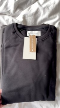 Sweatshirt preto de manga longa dobrado de forma organizada, com um decote redondo canelado e etiqueta de cuidados. Textura suave com um tecido leve.