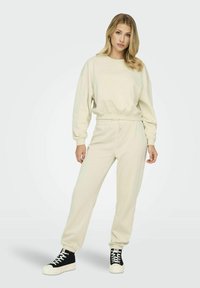 Completo sportivo color crema, composto da una felpa cropped con vita elastica e pantaloni jogger abbinati. Sneakers alte in bianco e nero.