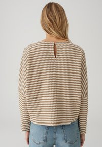 Maglione a righe beige e crema con dettaglio a foro sulla schiena, vestibilità morbida e maniche lunghe, abbinato a jeans blu a vita alta.