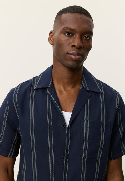 Chemise à manches courtes bleu marine avec des rayures verticales blanches et vertes. Comprend un col cranté, une poche poitrine et une fermeture à boutons.