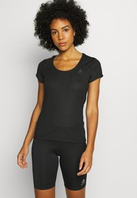 Black athletic shirt with short sleeves, scoop neck, and logo, paired with fitted black shorts. Fabric appears breathable and smooth.