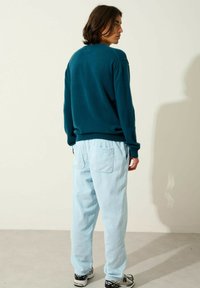 Un pull en teal avec une coupe décontractée et des poignets côtelés, associé à un pantalon en velours côtelé bleu clair avec des poches. Les chaussures sont des baskets noires et blanches.