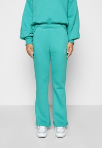 Turquoise sweatpants in a relaxed fit, made of soft material with a slightly flared shape, featuring a small logo detail on the side.